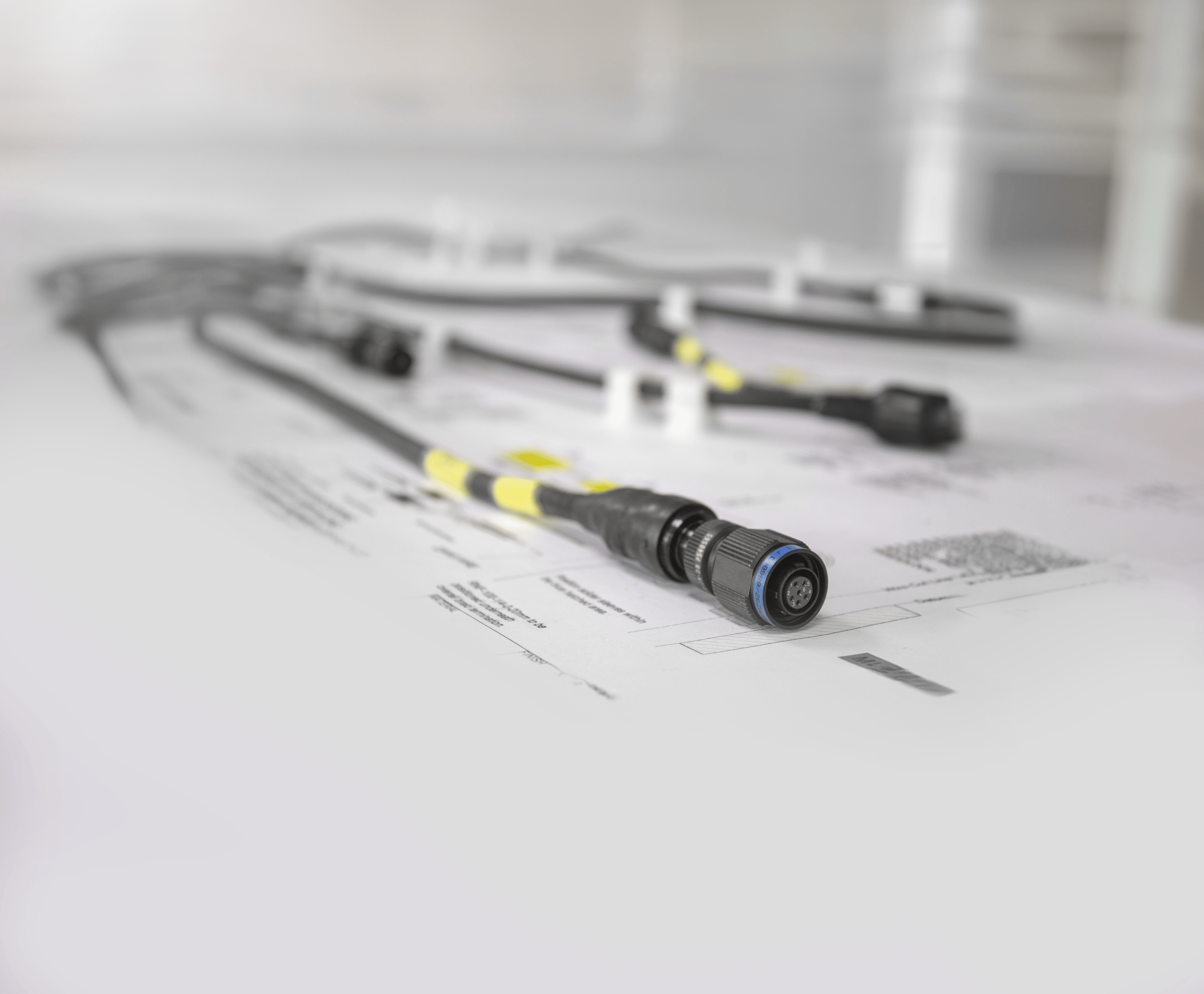 Close-up of a completed cable harness with a yellow and black banded circular connector, resting on engineering drawings at AQ Wiring Systems Rockford
